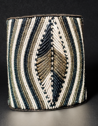 Beaded cylindrical container with feather design on a dark background