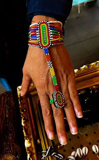 Hand wearing a colorful beaded bracelet and ring against a dark background